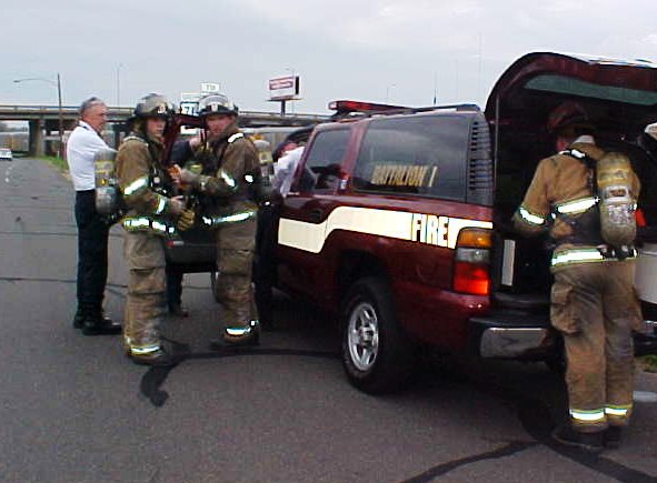 Fire fighters in full gear standing around their red SUV, waiting for instructions.